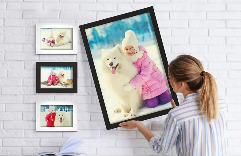 Cadre photo personnalisé : une femme accroche un grand tirage photo d’enfant et son chien Samoyède, entouré de photos plus petites.